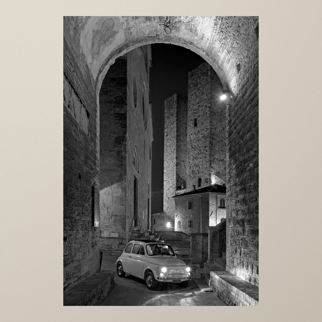 Between Towers and Shadows – A Fiat 500 parked under an arch below the night-lit towers of San Gimignano – photograph by Duccio Nacci
