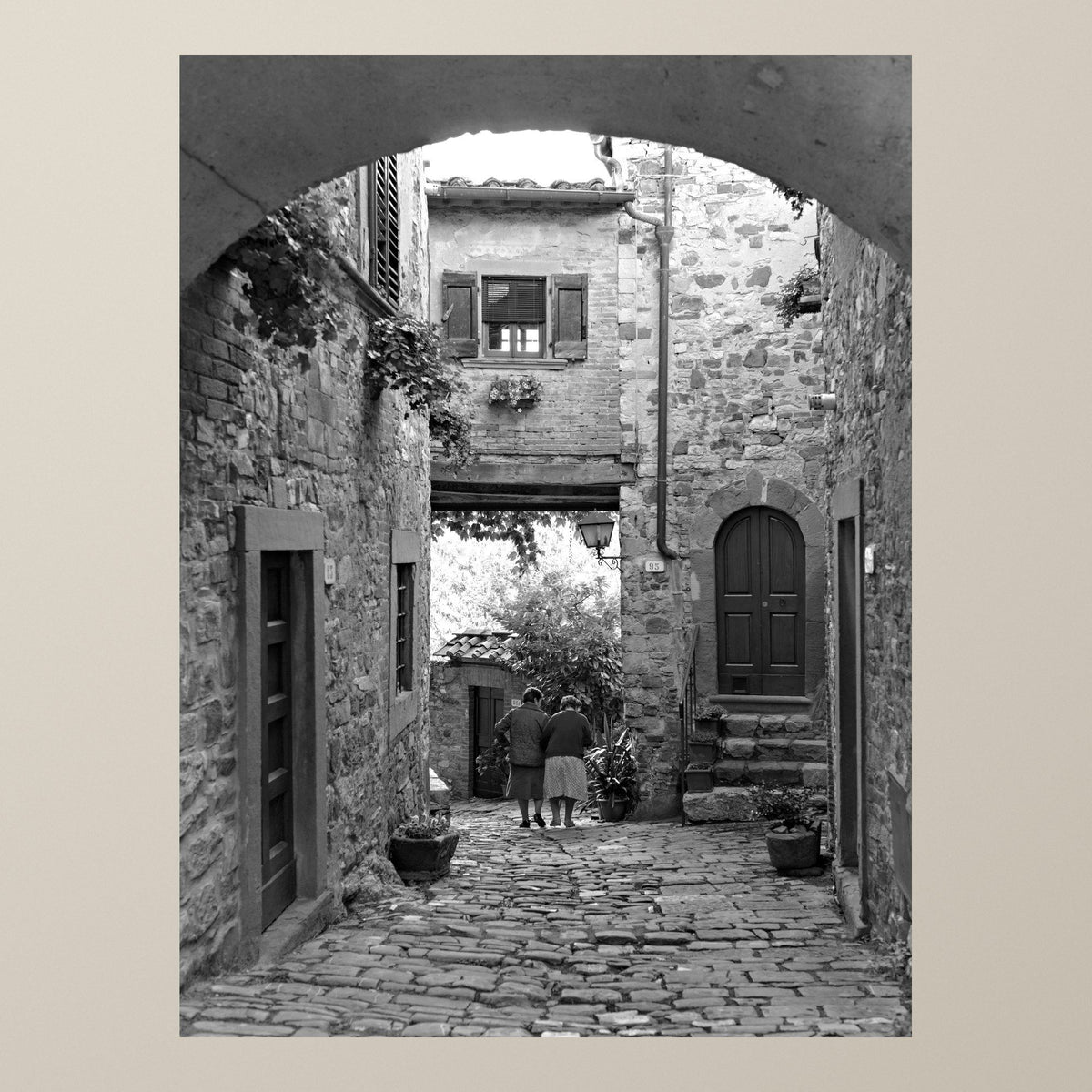 Eternal Friendship – Two figures walk together through an ancient stone alley of a Tuscan village – photograph by Duccio Nacci
