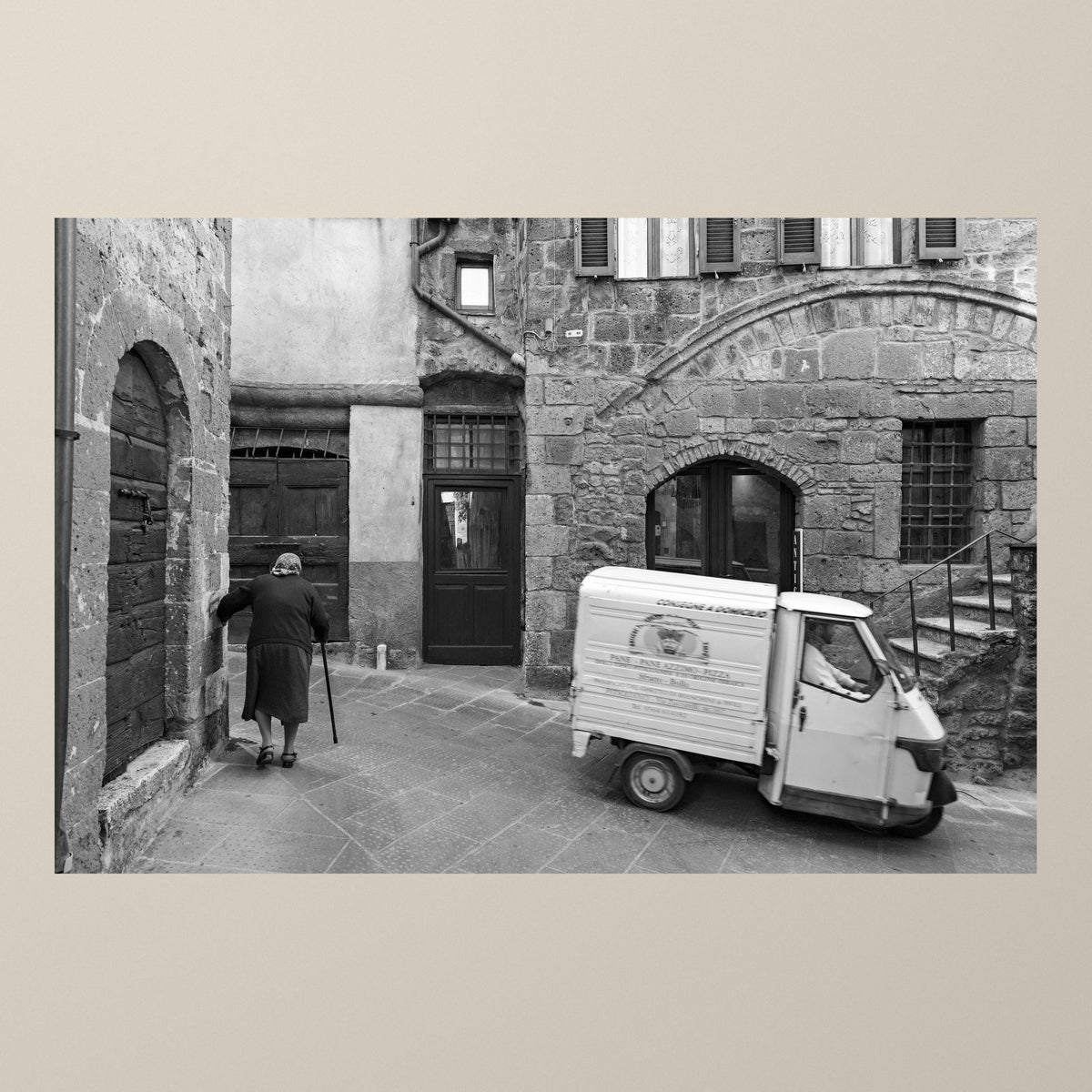 Everyday Eternity – A Piaggio Ape by ancient stone walls as an elderly woman walks by – photograph by Duccio Nacci