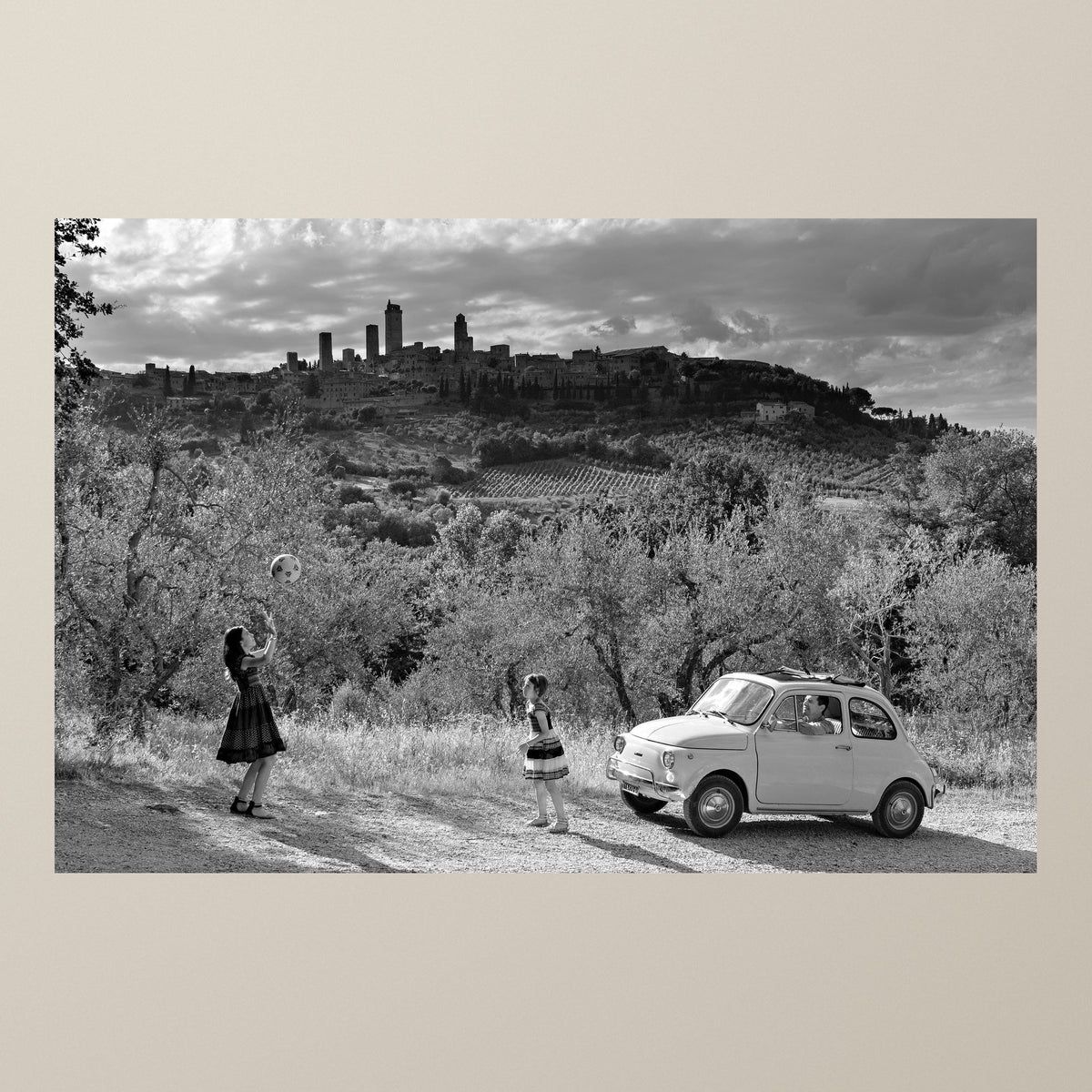 Italian Summer – Two girls play with a ball before San Gimignano, a white Fiat 500 nearby – photograph by Duccio Nacci