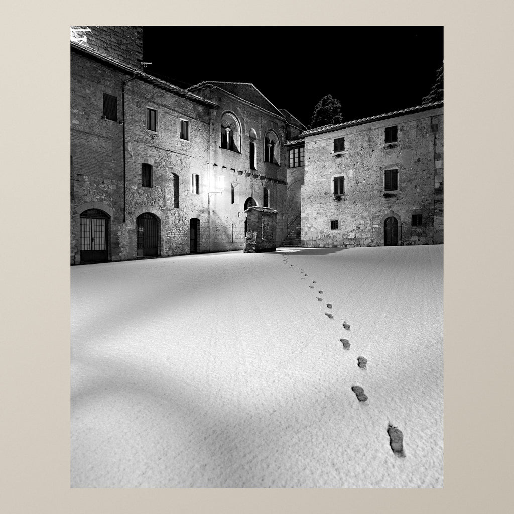 Steps in the Snow – Footprints in the snow across a medieval Tuscan courtyard in winter – photograph by Duccio Nacci
