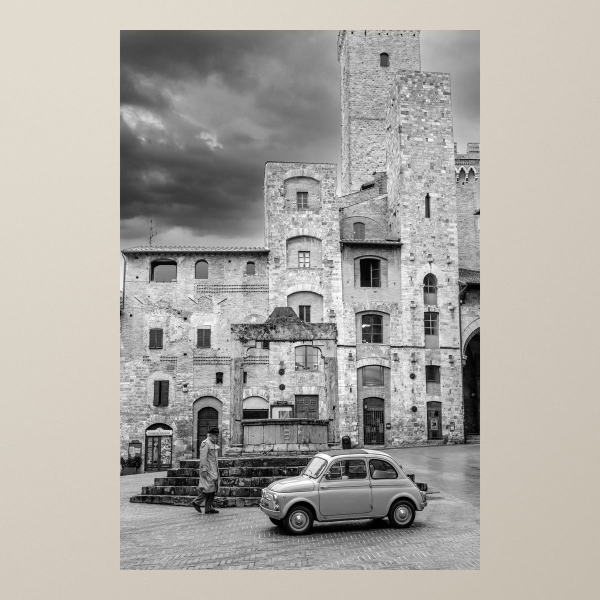 The Gentleman Stroll – A Fiat 500 before the towers of San Gimignano as a gentleman in a trenchcoat walks by – photograph by Duccio Nacci