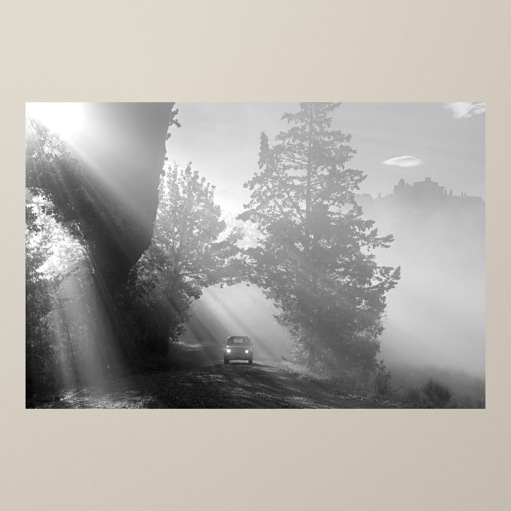 The Path of Light – Sunbeams break through trees and morning mist above a Fiat 500 on a Tuscan road – photograph by Duccio Nacci